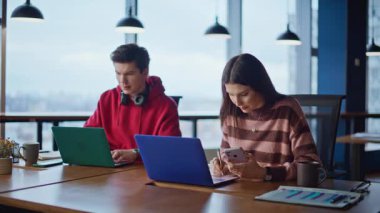 Çevrimiçi çalışan meslektaşlar yaratıcı açık alanda yakın plan çekimde oturuyorlar. Bilgisayarda yazı yazan genç iş arkadaşları ofiste iş birliği yapıyorlar. Pozitif erkek hippi kahve içen kadın akıllı telefonlara bakıyor..