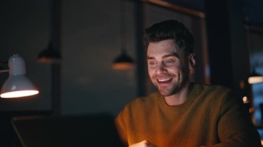 Mutlu gece vardiyası video görüşmeleri diz üstü bilgisayarlı web kamerasına yakın çekim. Gülümseyen serbest yazar, gece işyerinde online konferansın tadını çıkarıyor. Neşeli uzaktan kumandalı yönetici içeride dostça sanal toplantı yaptı.