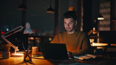 Gece kreatif ajans ofisinde başarılı bir yönetici. Gülümseyen işadamı bilgisayarında e-posta okuyor ve iş büyümesini düşünüyor. Mutlu Adam Serbest Çalışan Akşamüstü çevrimiçi Proje.