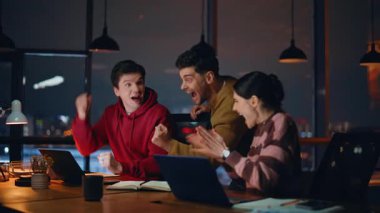 Coşkulu çalışanlar, akşam 5 'te iş yerinde yakın çekim yapmanın keyfini çıkarıyorlar. Mutlu meslektaşlar online olarak evet jestleri yaparak zaferi kutluyor. Heyecanlı iş adamları birlikte iş zaferini şaşırttı.
