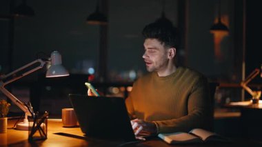 Uzaktan kumandalı yönetici gece iş yerinde cep telefonuna cevap veriyor. Gülümseyen adam cep telefonu sohbetini dizüstü bilgisayarla yapmaya başladı. Neşeli çalışan gece geç saatlerde akıllı telefondan konuşuyor..