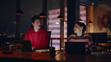 Bilgisayarlarda fazla mesai yapan gülümseyen meslektaşlar gece çalışma alanlarını kapatıyorlar. Şirket çalışanları online proje daktilo dizüstü bilgisayarlarına odaklandı. Profesyonel takım, gece geç saatlerde kapalı alanda başlangıç geliştiriyor..