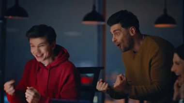 Heyecanlı takım, gece işyerinde başarıyı yakalıyor. Gülümseyen iş arkadaşları iş başarısına sevinerek karanlık ofiste beşini bir arada veriyor. Mutlu meslektaşlar içeride başarılı takım çalışmalarından zevk alıyor..