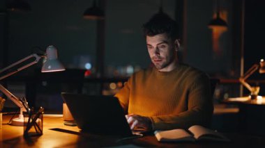 Serbest çalışan dizüstü bilgisayarı akşam üzeri yakın çekim alanında programlıyor. Ciddi bir işletme yöneticisi bilgisayarda fazla mesai işine odaklanmış görünüyor. Uzaktan gece ofisinde çalışan profesyonel bilişim işçisi..