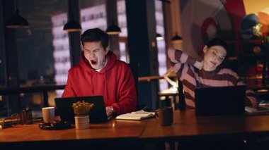 Uykulu iş arkadaşları karanlık iş yerinde fazla mesai yapan dizüstü bilgisayarlara bakıyor. Çok çalışan iş arkadaşları geç saatlere kadar çalışmaktan boynunu esnetiyorlar. Yorgun adam çevrimiçi bilgisayar aşırı yüklenmesi projesini kapatıyor.