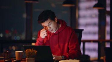 Karanlık çalışma alanında çalışan yorgun iş arkadaşları yakın plan çekimde. İki çalışanın dizüstü bilgisayar izlemesi gece ofisinde gerginlik yaratıyor. Çok çalışan adam bilgisayarını kapatıyor. Kadın el saatine bakıyor..