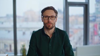 Sakallı yönetmen iş yerinde poz veriyor. Modayı takip eden siyah tişörtü giyiyor. Gözlüklü yakışıklı işadamı, kendine güvenen bir gülümseme ile kameraya bakıyor. Zengin işletme sahibi modern ofis alanında oturuyor..