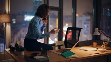 İşkolik konuşan mutlu cep telefonları karanlık çalışma masasında oturup dizüstü bilgisayarın verilerine bakıyor. Gülümseyen iş kadını cep telefonuyla başarılı projeyi tartışıyor. Neşeli bayan yönetici gece akıllı telefonu arıyor.