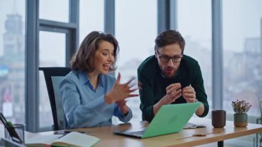 Heyecanlı yöneticiler ofiste dizüstü bilgisayara bakarken panoramik pencereyi kapatarak başarıyı kutluyorlar. Coşkulu iş adamları başarıya seviniyor. Mutlu iş arkadaşları iş yerinde duygusal kazanç üzerine tepki veriyorlar.