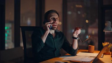 Karanlık ofisteki çalışma masasında dizüstü bilgisayarla gülen acemiyi aramak. Gülümseyen iş adamı akşam geç saatlerde keyifli telefon görüşmelerinin tadını çıkarıyor. Mutlu yönetici gece haberlerini cep telefonuyla paylaşıyor..