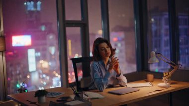 Motivasyonsuz çalışan gece işyerinde kendini tükenmiş hissediyor. Yorgun iş kadını dizüstü bilgisayar açıyor karanlık ofiste fazla mesai yapıyor sokak lambaları şehir manzaralı. Bunaltıcı yönetici tarama bilgisayarı.