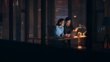 Lamba ışığında dizüstü bilgisayarda çalışarak fazla mesai yapan iki profesyonel. Gülümseyen meslektaşlar birlikte online girişim geliştiriyorlar. Hevesli personel iş planını tartışıyor.