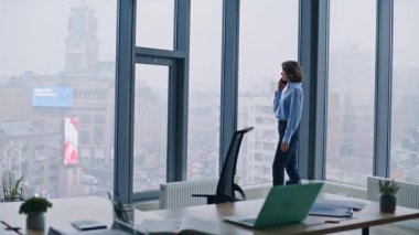 Ofis panoramik penceresinde konuşan şık bir yönetici. Zarif bir iş kadını cep telefonunu arıyor modern lüks işyerinde duruyor. Başarılı bayan patron işi akıllı telefon görüşmesi..