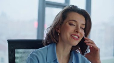 Şirket işyerinde cep telefonunu arayan neşeli iş kadını portresi. Gülümseyen kadın CEO modern ofiste oturarak akıllı telefonla pazarlık yapıyor. Güzel bayan patron cep telefonundan konuşuyor..