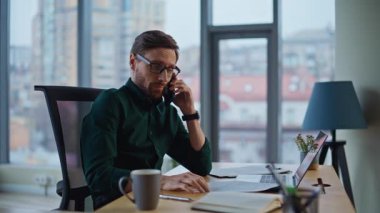 Endişeli yönetici iş yerinde cep telefonuyla konuşuyor ve dizüstü bilgisayarını kapatıyor. Endişeli iş adamı iş meselelerini cep telefonuyla açıklıyor. Sorunlu CEO 'nun gözlüklerini çıkarması sorunu akıllı telefondan tartışır..