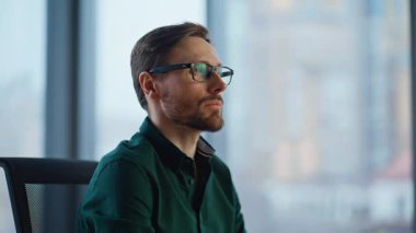 Ofis ışıklarının altında oturan kendine güvenen iş adamı gözlük takıyor. Modern işyerinde kameraya gülümseyen sakallı girişimci. Panoramik pencere tarafından poz veren başarılı yönetici yönetici.