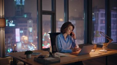 Endişeli iş kadını, parlak şehir manzaralı karanlık ofisten arıyor. Endişeli kadın yönetici cep telefonuyla proje sorununu tartışıyor. Zarif yönetici akıllı telefondan işten şikayet ediyor.