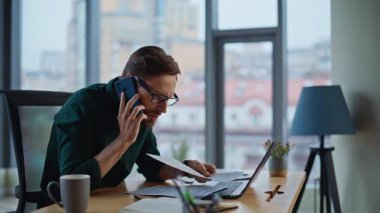 Stresli yatırımcı cep telefonuyla bağırarak ofiste kötü mali raporları okuyor. Sinirli iş adamı cep telefonuyla bağırıyor. Sinirli patron gerilimi hissederek akıllı telefon konuşmasını bitirdi.