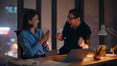 Heyecanlı ortaklar, gece ofisindeki dizüstü bilgisayarla kazandıkları için seviniyorlar. Gece geç saatlerde iş başarısını kutlayan aşırı neşeli iş ekibi. Duygusal meslektaşlar harika e-posta haberleri okuyorlar..