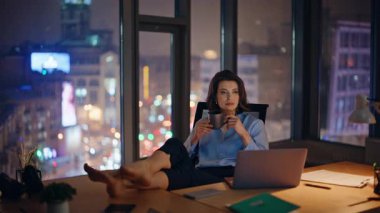 Fazla mesai yapan rahat bir işçi gece ofisinde dinleniyor. Çıplak ayakla çalışma masasına oturuyor. Kahve fincanı tutan zarif iş kadını iş gününün sonunda eğleniyor. Sakin kadın yönetici karanlık işyerinde içecekle rahatlıyor..