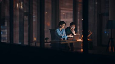 Çalışkan iş adamları karanlık ofisteki bilgisayarlara göz atıyorlar. Gülümseyen iş kadını gece vakti iş adamına online proje sunuyor. Şirket geliştirme fazla mesaisinde çalışan mutlu meslektaşlar.