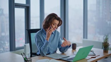 Şirket çalışanı cep telefonuyla konuşuyor modern işyerinde oturuyor dizüstü bilgisayarı yakından izliyor. Gülümseyen iş kadını iş ortağını arıyor. Zarif kadın çalışan cep telefonuyla projeyi tartışıyor.