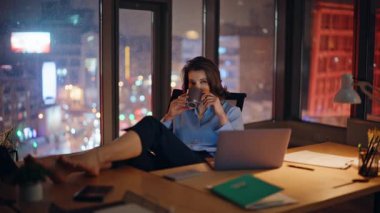 Sakin bir iş kadını, modern bir ofiste kahve içiyor. Şık bir yönetici kadın içki yudumlarken mesaiye ara veriyor. Rahatlamış CEO, iş yerinde çıplak ayakla dinleniyor..