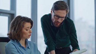 Erkek amir, şirket ofisinde kadın yöneticiyle evrakları tartışıyor. Memnuniyetsiz yönetici mali rapordan muhasebeciye şikayet ediyor. İki meslektaş iş belgelerini inceliyor.