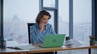 Gülümseyen iş kadını iş yerindeki gazeteleri kontrol etmek için cep telefonunu arıyor. Pozitif iş kadını cep telefonu görünümlü dizüstü bilgisayar konuşuyor. Kendine güvenen kadın yönetici, müvekkil okuyucu belgesine danışıyor.