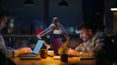 Modern çalışma alanındaki bilgisayarlarda çalışan gece çalışanları. Takım lideri kadın, akşam lambası kabinesinde fikir alışverişinde bulunan iş arkadaşlarını getiriyor. Şirket çalışanları içeride beyin fırtınası yapıyor.