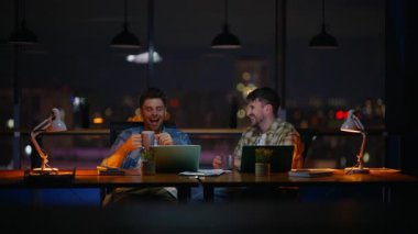 Kahkaha eşleri gece kahve fincanları tutarak iş yerinde dinleniyorlar. İki pozitif adam ara vermenin tadını çıkarıyor. Dost canlısı tasarımcıların teslim tarihi karanlık ofisi gevşetiyor. Kurumsal iş hayatı