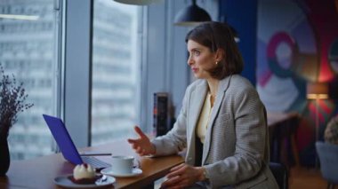 Yaratıcı tasarımcı, çağdaş kafe kapanışında bilgisayar istiyor. Gülümseyen sanal asistan modern barda oturmuş bilgisayar kamerasından konuşuyor. Uzak iş toplantısında mutlu stil sahibi iş kadını 