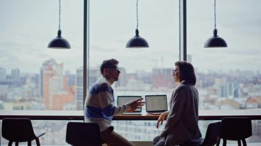 Şehir merkezindeki iş arkadaşları yakın planda oturuyor. Ciddi meslektaşlarım panoramik pencere odasında girişimi tartışıyor. Gözlüklü kadın menajerler iş yerinde iletişim kuruyor. İki kişi konuşuyor.