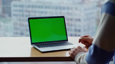 Kimliği belirsiz adam yeşil ekran dizüstü bilgisayar izliyor. Şehir manzaralı evde video dersi veriyor. Modern bilgisayarda modelleme görüntüsüyle tanınmayan bir adam arıyor. Serbest Çalışmacı uzak çalışma için teknolojiyi kullanıyor
