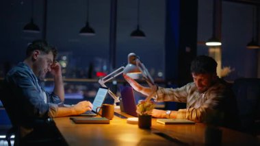Karanlık ofiste fazla mesai yapmaktan yorgun düşmüş gece çalışanları. Yorgun takım arkadaşı işi bitirme günü bilgisayarını kapatıyor. Son teslim tarihi baskısı altında iş birliği yapan iki iş arkadaşı.