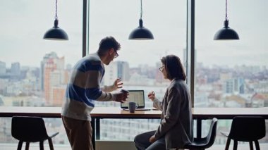 İş arkadaşları büyük pencerelerin önünde dizüstü bilgisayarla ilgili konuşuyorlar. Panoramik Ofis 'te erkek partner dinleyen zarif bir kadın. Profesyonel çiftler birlikte kahve fincanlarıyla proje hazırlıyorlar.
