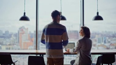 Erkek işçi, kadın meslektaşını karşılıyor. Geniş bir pencerenin arkasında sohbet ediyorlar. Laptoplarda çalışan iki dost canlısı çalışan birlikte iletişim kuruyor. Yaratıcı ajansta çalışan pozitif yöneticiler.