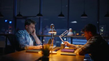 Çok çalışan meslektaşlar ofis odasında son teslim tarihine hazırlanıyor. Lamba ışığında kendini yorgun hisseden iki adam yüzlerini ovuşturuyor. Yaratıcı gece içlerinde geç saatlere kadar birlikte çalışmaktan yorulmuş serbest çalışanlar.