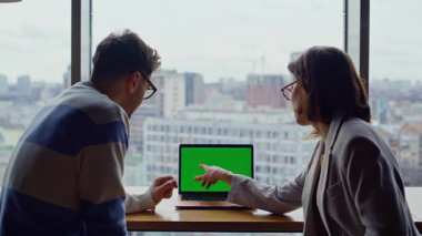 Cam duvarlar ofis dikiz aynasındaki krom anahtar cihazında çalışan iki çalışan. İki iş adamı açık alanda dizüstü bilgisayarla sohbet ediyor. Yeşil ekran bilgisayarını işaret eden meslektaşlar birlikte konuşuyor 