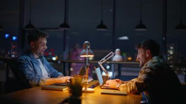 Karanlık kabinede sohbet eden pozitif gece işçileri. Tasasız takım arkadaşları iş yerinde dizüstü bilgisayar şakası yapıyor. Neşeli tasarımcılar lamba ışığında birlikte konuşuyor. Bilgisayarda çalışan adamlar