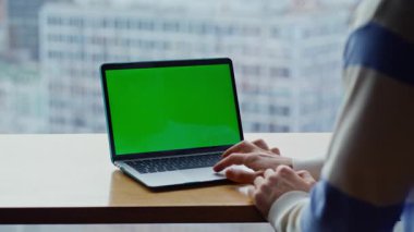 Şehirdeki uzak iş yerindeki krom tuşlu bilgisayara dokunan bir adam. Yeşil ekran dizüstü bilgisayar kullanarak tanınmaz hale geldi. Açık alan panoramik ofisinde çalışan bilinmeyen yönetici 