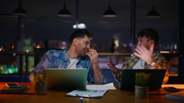 Akşam müdürleri yakın plan çekimde eğleniyorlar. Geç saatte iş yerinde gülen iki meslektaş. Mutlu denetçiler iş yerinde gayri resmi iletişimin keyfini çıkarıyorlar. 