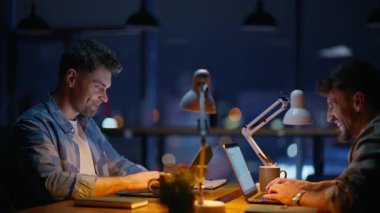 Neşeli tasarımcılar gece ofislerini kapatıyorlar. Kaygısız mürettebat iş yerinde şaka yaparken eğleniyor. İş ekibi sıcak ışık akşam odasında konuşuyor. Bilgisayarda çalışan adamlar