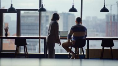 Erkek kadın dizüstü bilgisayara bakıyor panoramik şehir manzarası işyerinde proje tartışıyorlar. Çağdaş ofiste para kaybeden iş arkadaşları umutsuzluğa kapıldılar. İş ortakları üzücü iş başarısızlığı