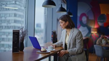 Modern kafeteryadaki bilgisayarla online çalışan zarif bir öğrenci. Resmi takım elbiseli, kendine güvenen esmer kadın kafeden arıyor. Duygusal iş kadını sanal toplantı jestinde danışmanlık yapıyor. 