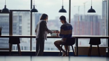 Ofis arkadaşları şık bir iç mekanda kahve molası veriyorlar. Takım üyeleri modern çalışma alanı salonundaki şehir manzarası projesinde işbirliği yapıyorlar. Zarif lider kadın iş arkadaşına sıcak kapuçino getiriyor.