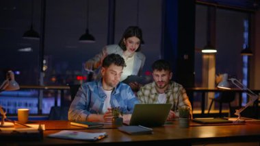 Akşam takım arkadaşları modern panoramik iş yerinde laptopu görüntülüyorlar. Meslektaşlarını temsil eden profesyonel kadın takım lideri. İçerideki sanal toplantıda neşeli bir başlangıç grubu selamlaması