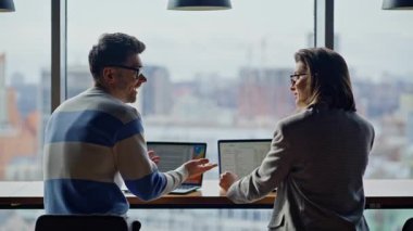 Neşe dolu takım arkadaşları panoramik birlikte çalışıyorlar. Bilgisayarlara bakan olumlu yaratıcı ajans çalışanları kapalı alandaki iş görevlerini tartışıyor. Geniş pencerelerde dizüstü bilgisayarlar yazan erkek kadın.