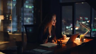 Modern çalışma alanlarında gece vardiyasında çalışan mutlu çalışanlar sohbet ediyor. Kendine güveni tam bir video konferansında dizüstü bilgisayarla gülümsüyor. Uzaktan çalışan bir işçi sakince dijital konferansa katılıyor.