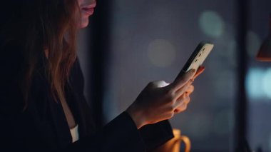 Akşam apartmanında elinde cep telefonu olan bir kadın. Akıllı telefondan sosyal medyayı izleyen mutlu gülümseyen kadın gece işyerinde oturuyor. Neşeli esmer, karanlık ofiste cep telefonuyla mesajlaşmayı sever. 
